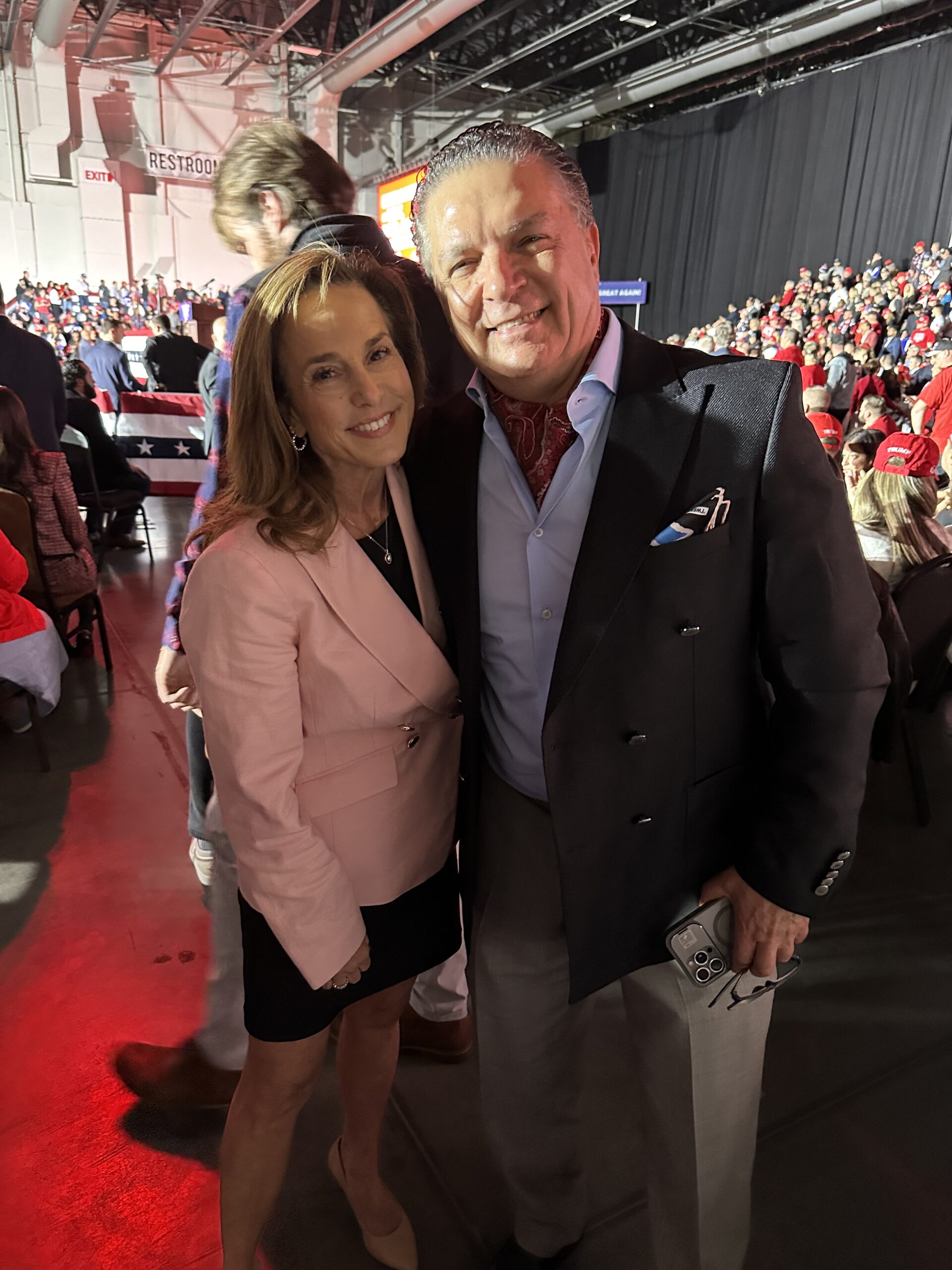 A smiling woman in a pink blazer and a man in a black suit pose together